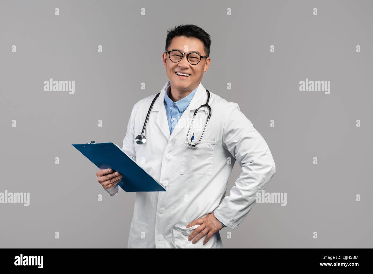 Portrait d'un médecin asiatique adulte confiant et heureux en manteau blanc, lunettes avec stéthoscope et tablette regarder l'appareil photo Banque D'Images