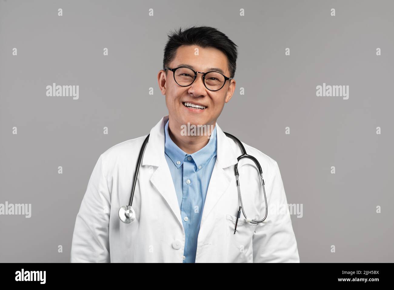 Bon thérapeute japonais d'âge moyen en manteau blanc, lunettes avec stéthoscope regarder la caméra Banque D'Images