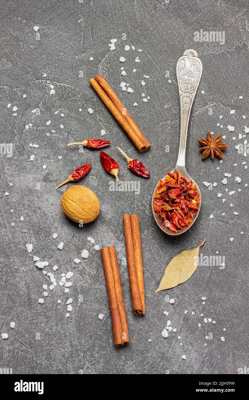 Séchez les poivrons dans une cuillère en métal, les gousses de poivre et les bâtonnets de cannelle sur la table. Copier l'espace. Pose à plat. Arrière-plan noir Banque D'Images