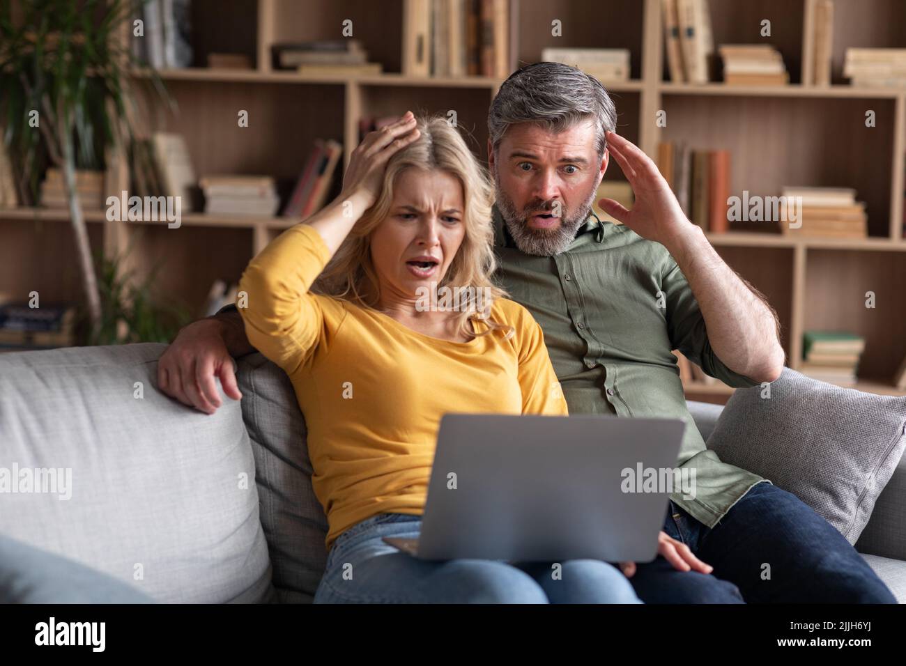 Escroquerie en ligne. Couple d'âge moyen et émotionnel regardant l'écran d'un ordinateur portable avec un choc Banque D'Images