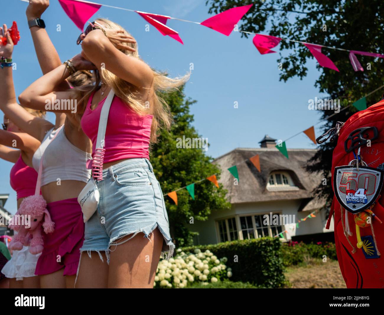 Deux femmes portant du rose applaudissent les marcheurs lors du plus grand événement de marche de plusieurs jours au monde. La marche des quatre jours (en néerlandais 'Vierdaagse') est considérée comme le premier exemple de l'esprit sportif et des liens internationaux entre militaires et civils de nombreux pays différents. Après deux ans d'annulation, il a été retenu à nouveau, mais le premier jour a été annulé en raison de températures chaudes, transformant les quatre marches en trois jours de marche. Il s'agit de l'édition 104 et le total officiel des marcheurs enregistrés était de 38 455 dans 69 pays. Ils peuvent choisir de marcher 30km, 40km ou 50km par jour. Banque D'Images