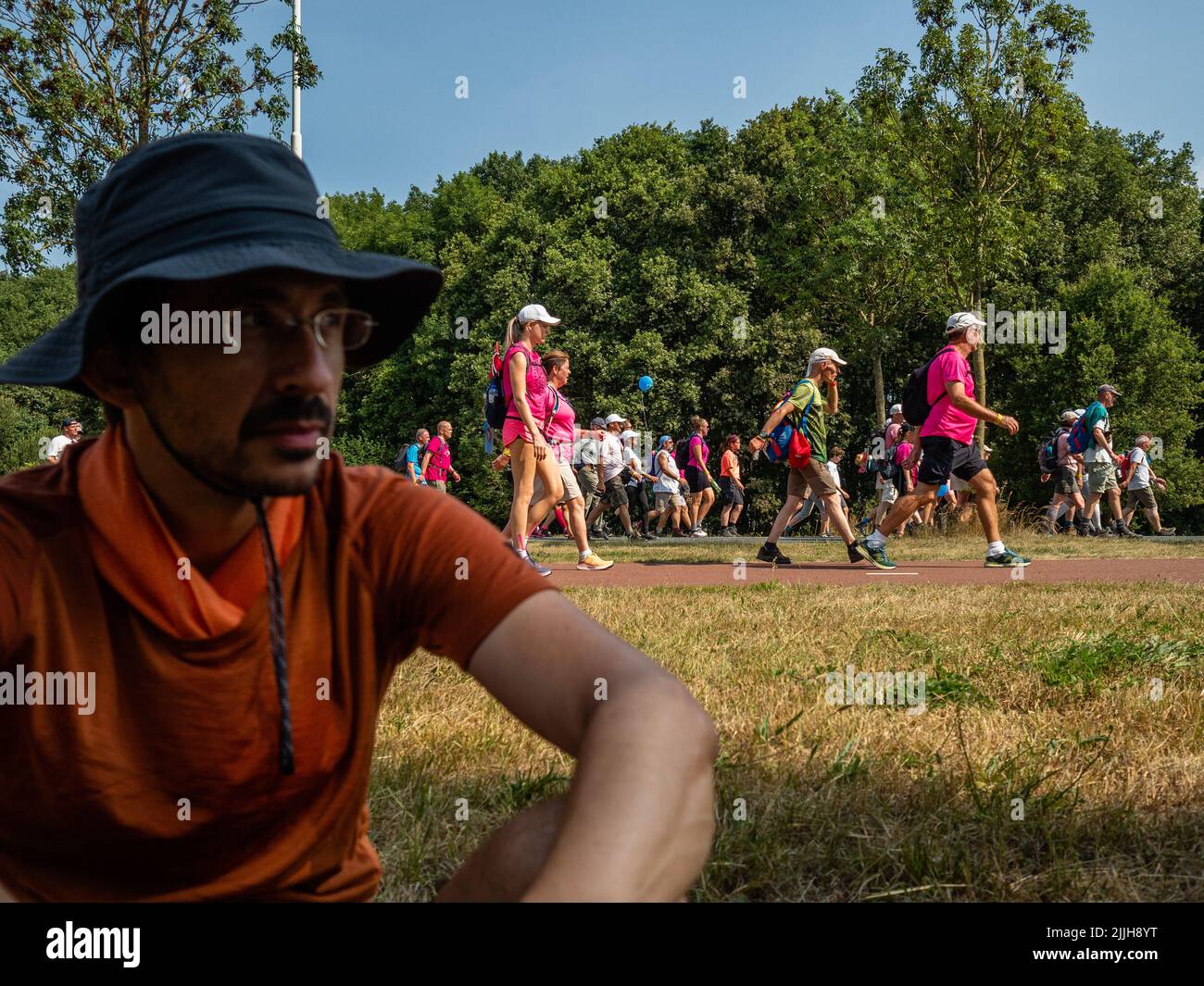 Un participant prend un repos pendant que d'autres continuent la marche pendant le plus grand événement de marche de plusieurs jours au monde. La marche des quatre jours (en néerlandais 'Vierdaagse') est considérée comme le premier exemple de l'esprit sportif et des liens internationaux entre militaires et civils de nombreux pays différents. Après deux ans d'annulation, il a été retenu à nouveau, mais le premier jour a été annulé en raison de températures chaudes, transformant les quatre marches en trois jours de marche. Il s'agit de l'édition 104 et le total officiel des marcheurs enregistrés était de 38 455 dans 69 pays. Ils peuvent choisir de marcher 30km, 40km ou 50km p. Banque D'Images