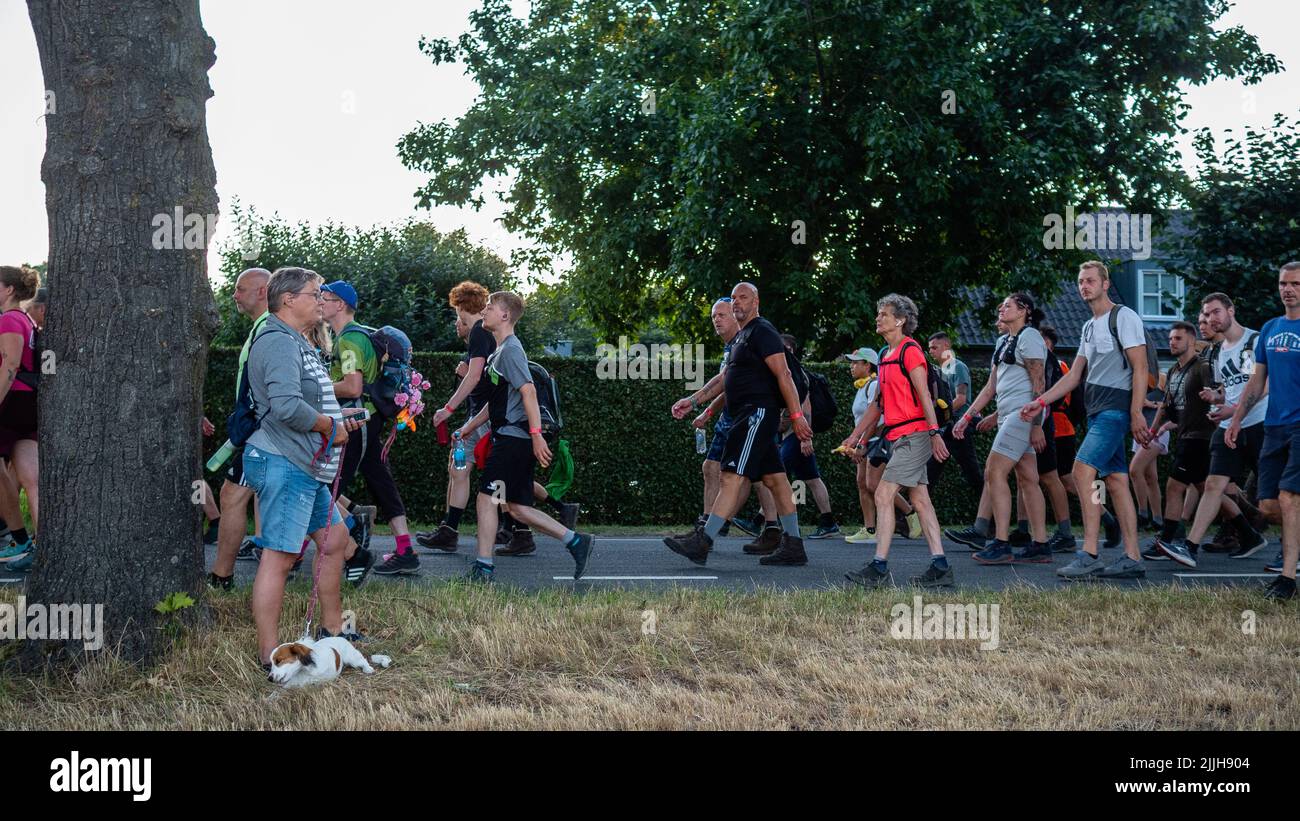 Une femme avec son chien pendant que d'autres participants marchent à pied pendant le plus grand événement de randonnée de plusieurs jours au monde. La marche des quatre jours (en néerlandais 'Vierdaagse') est considérée comme le premier exemple de l'esprit sportif et des liens internationaux entre militaires et civils de nombreux pays différents. Après deux ans d'annulation, il a été retenu à nouveau, mais le premier jour a été annulé en raison de températures chaudes, transformant les quatre marches en trois jours de marche. Il s'agit de l'édition 104 et le total officiel des marcheurs enregistrés était de 38 455 dans 69 pays. Ils peuvent choisir de marcher 30km, 40km ou 50km par jour Banque D'Images