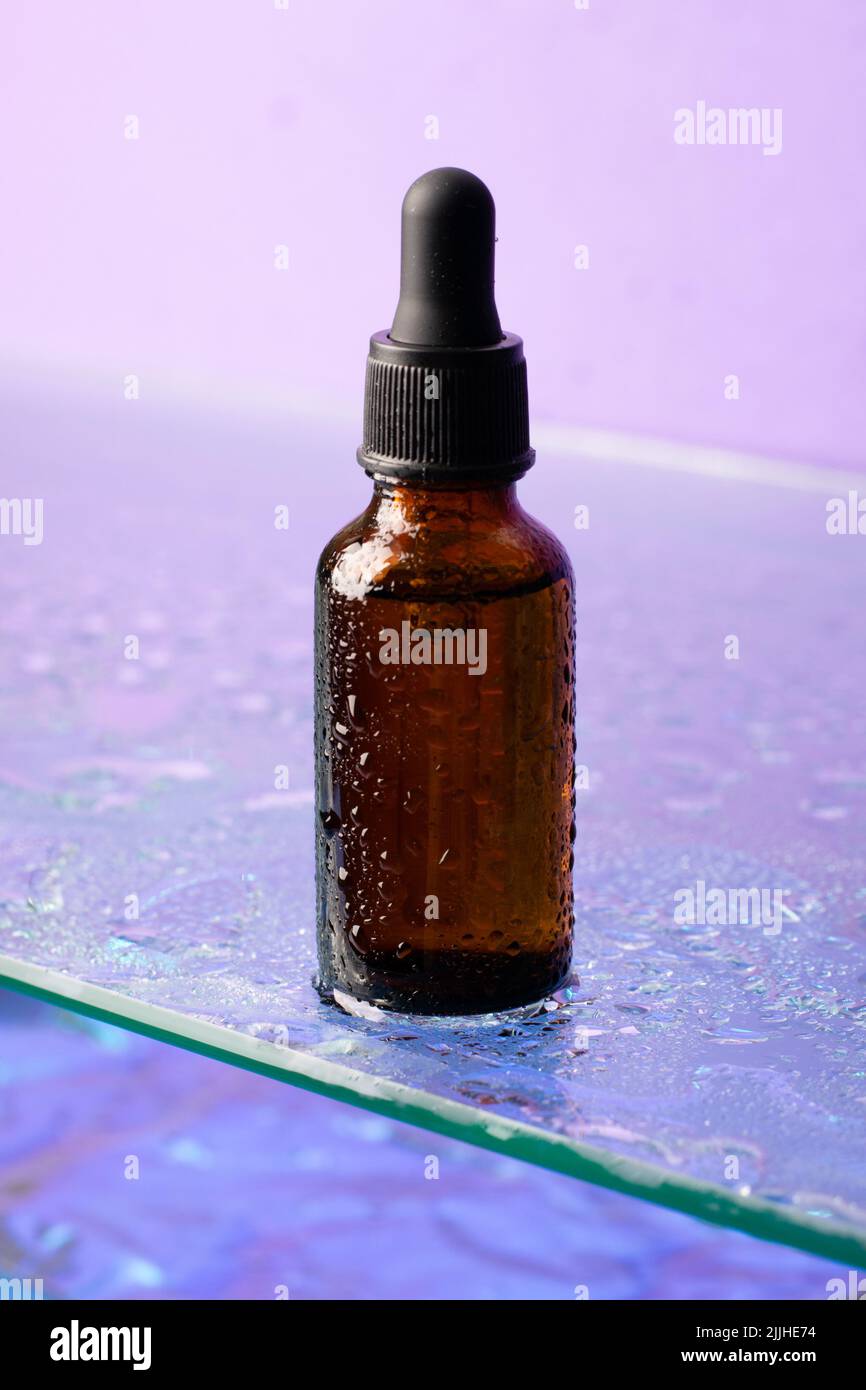 Bouteille de produit cosmétique, verre foncé avec pipette sur étagère en verre, fond violet, regarder vers le haut Banque D'Images