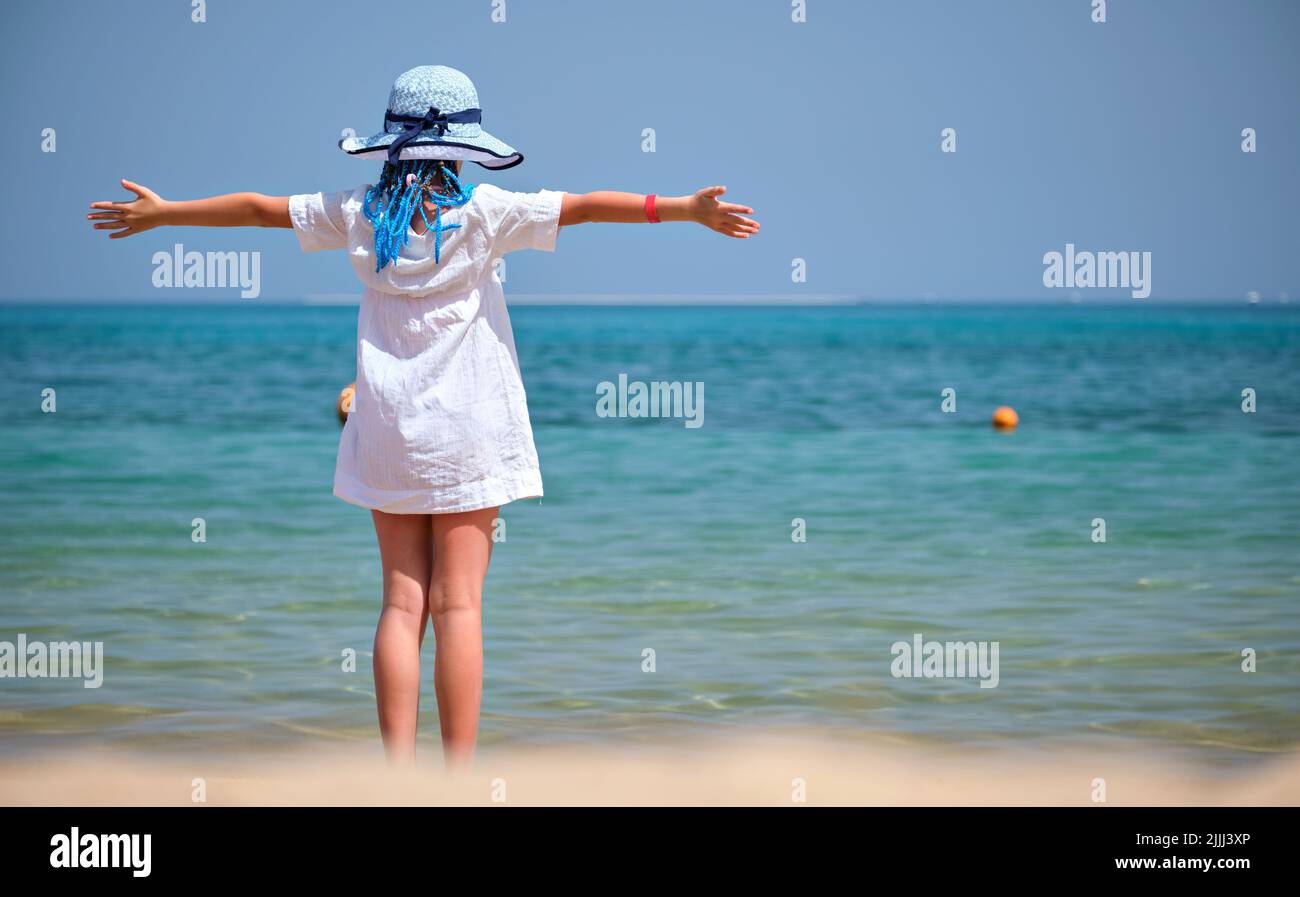 Vue arrière de l enfant fille en robe blanche et chapeau pieds nus avec les bras levés sur la