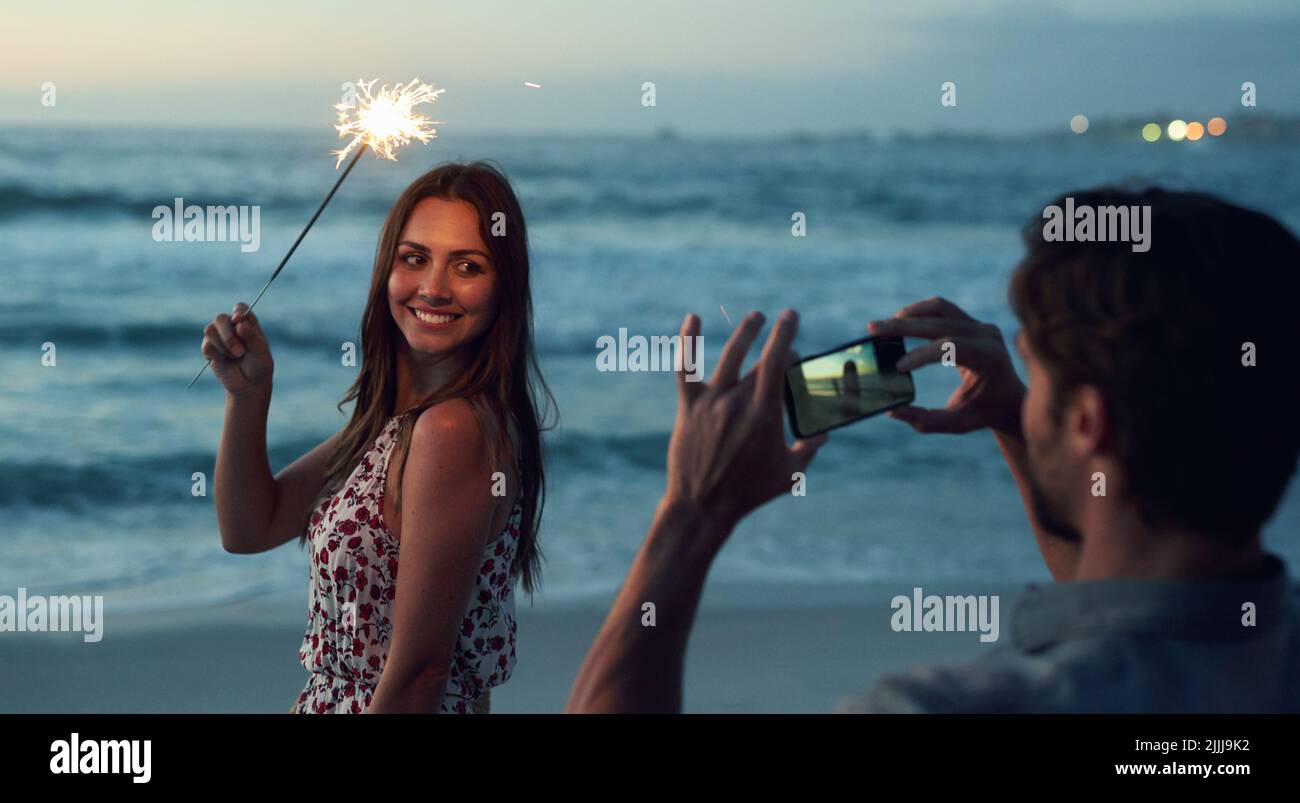 Belle femme tenant le sparkler posant pour la photo sur la plage romantique célébrant la Saint-Sylvestre au coucher du soleil Banque D'Images