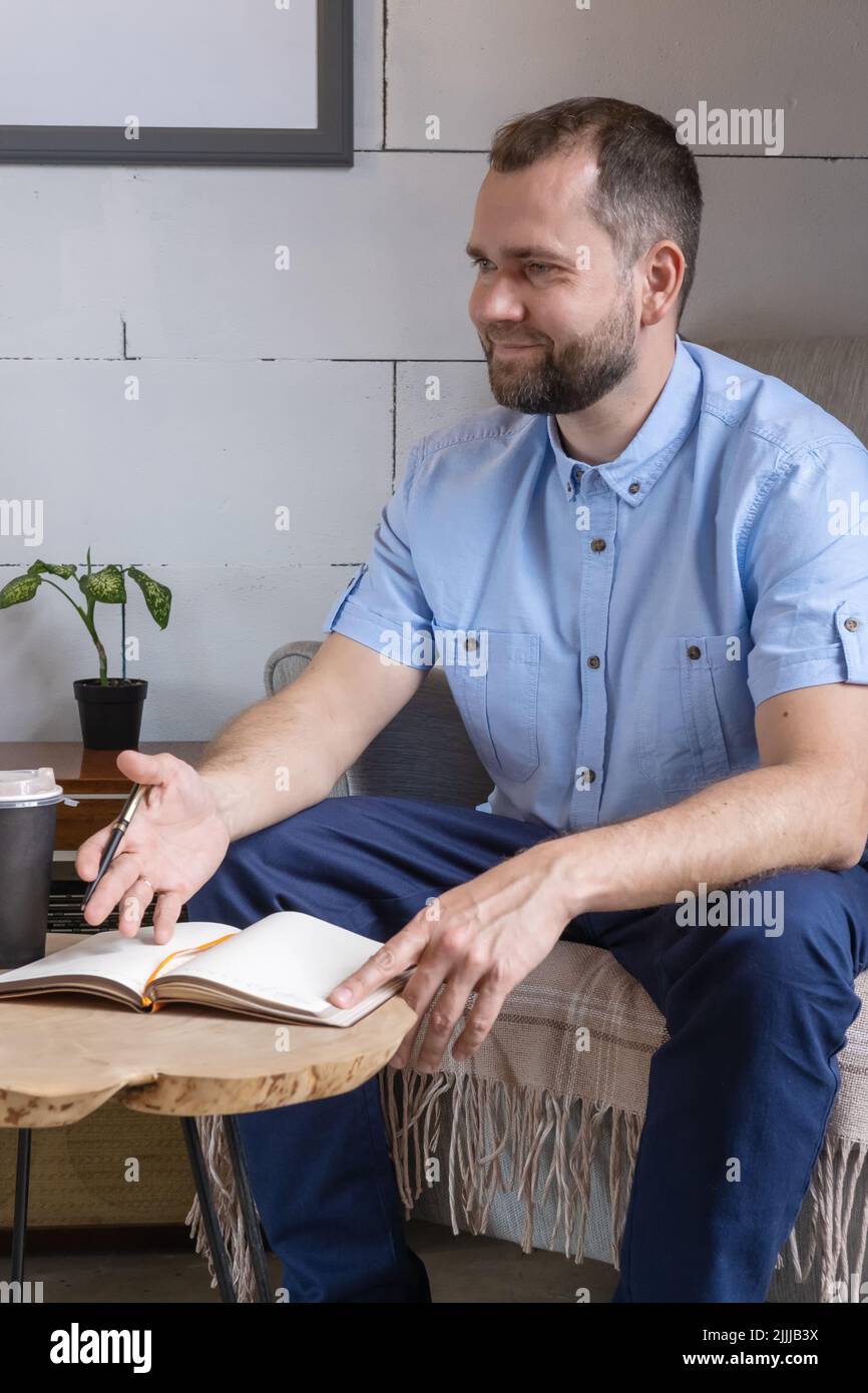 Un arabe d'âge moyen dans un costume d'affaires parlant à une table de café. Homme d'affaires souriant écrivant des notes dans un journal personnel, planifiant la journée de travail Banque D'Images