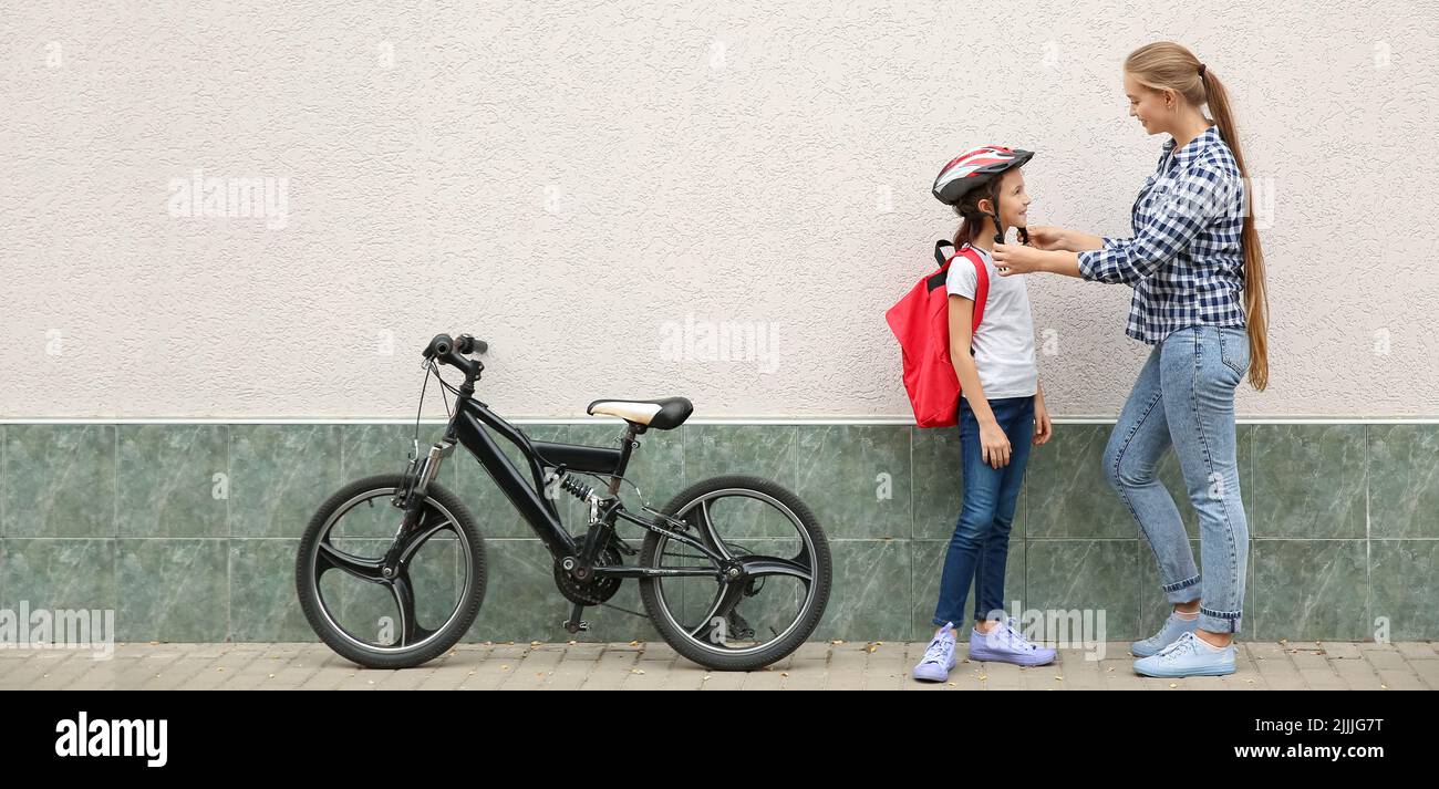 Mère aidant une petite écolière à mettre un casque de vélo à l'extérieur Banque D'Images