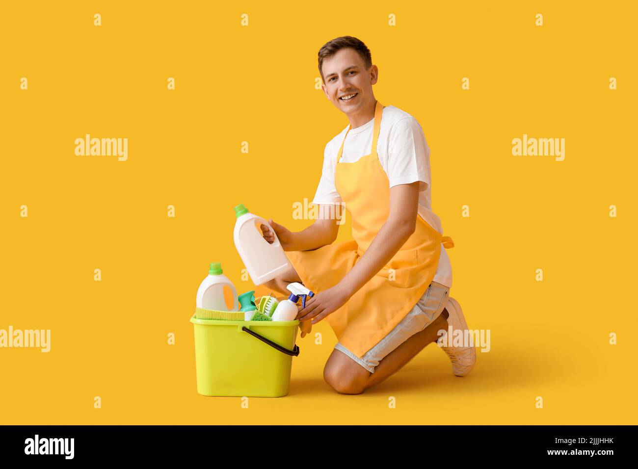 Jeune homme et seau avec fournitures de nettoyage sur fond jaune Banque D'Images