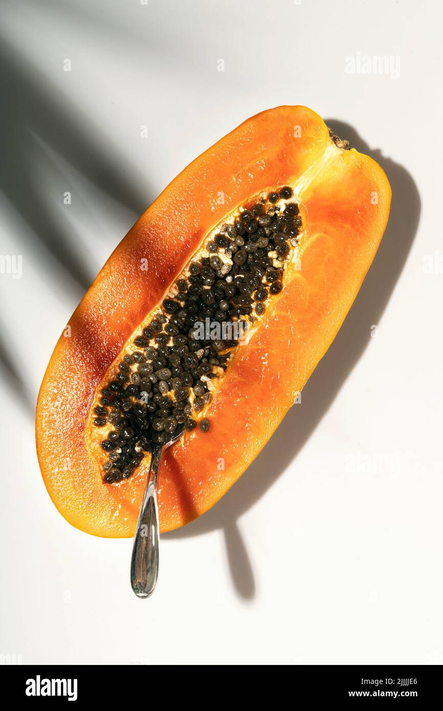 Papaye sur fond blanc avec ombre de feuilles de palmier, concept alimentaire créatif, fruits tropicaux. Pose à plat. Banque D'Images