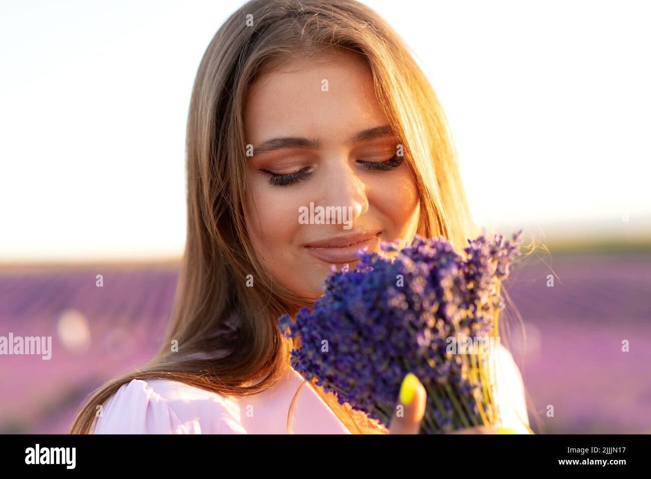 Jeune femme en robe tenant un bouquet de fleurs debout dans le champ de lavande Banque D'Images