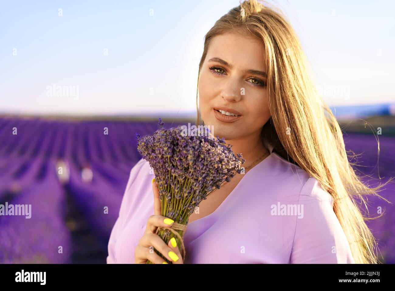 Jeune femme en robe tenant un bouquet de fleurs debout dans le champ de lavande Banque D'Images