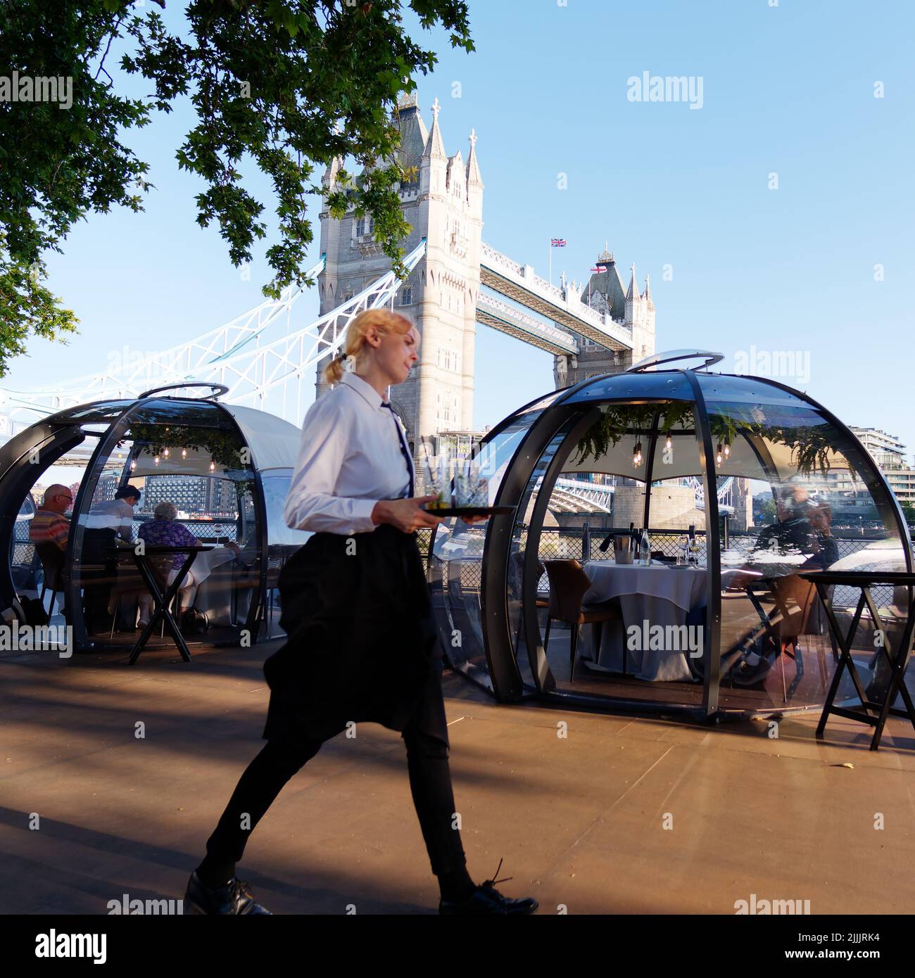 Londres, Grand Londres, Angleterre, 22 juin 2022 : la serveuse porte un plateau de boissons au restaurant Glass Rooms avec Tower Bridge derrière. Banque D'Images