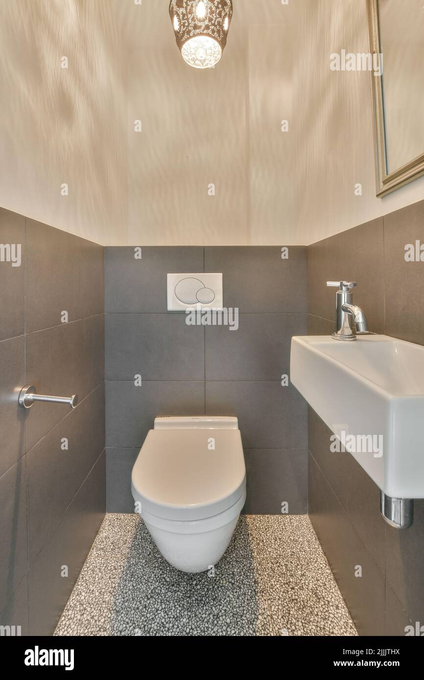 toilettes modernes installées sur un mur beige sous le bouton et éclairées étagère dans les toilettes légères à la maison Banque D'Images