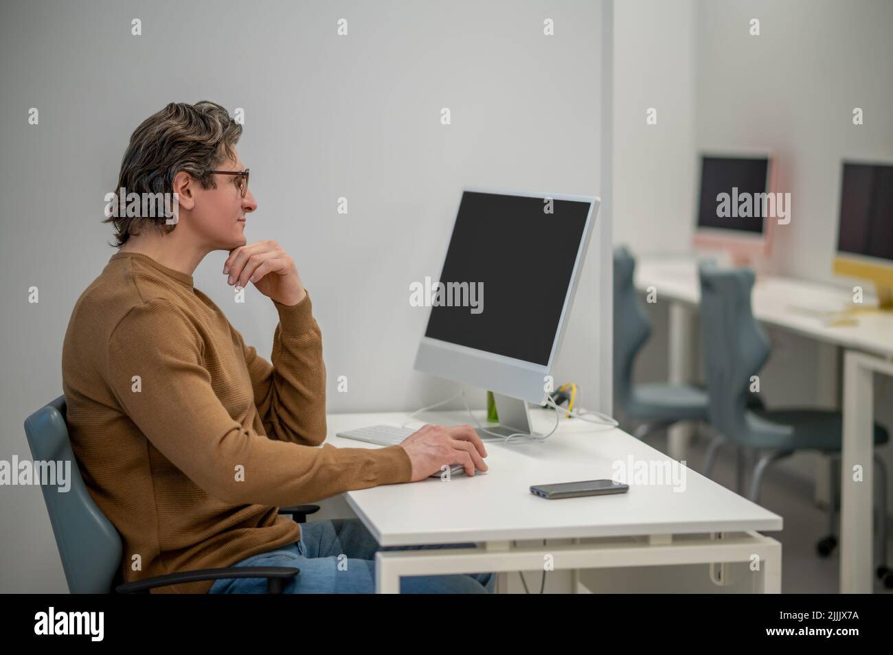 Un homme aux cheveux sombres assis à l'ordinateur et regardant impliqué Banque D'Images