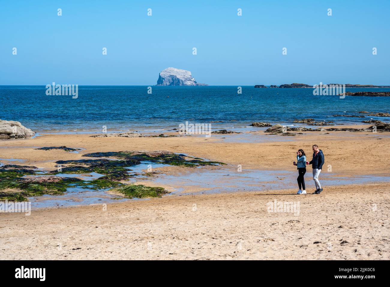 Jeune couple bénéficiant du soleil de printemps sur la plage de Milsey Bay, avec le Bass Rock au loin, North Berwick, East Lothian, Écosse, Royaume-Uni Banque D'Images
