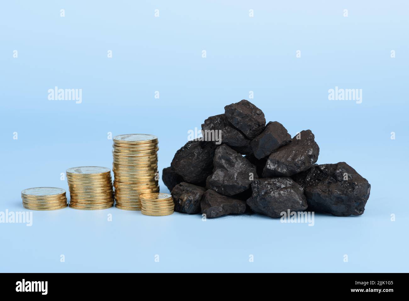 Charbon dur noir avec piles de pièces sur fond bleu, concept de prix des combustibles fossiles Banque D'Images