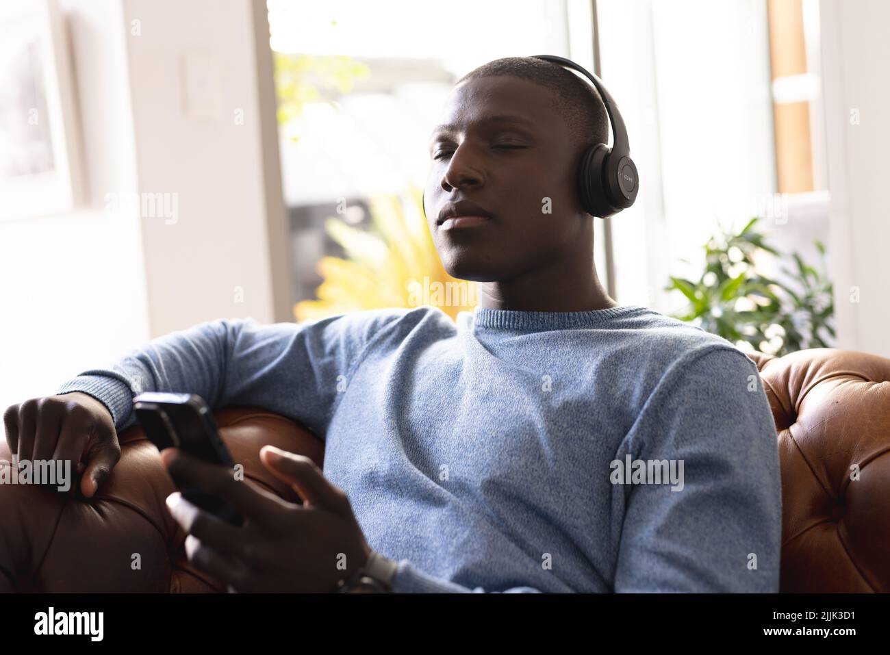 Homme afro-américain de taille moyenne, avec les yeux fermés, écoutant de la musique dans un casque et se détendant à la maison Banque D'Images