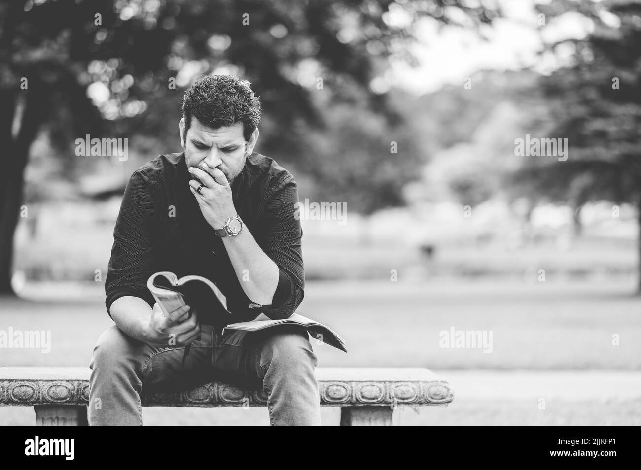 Un gros plan d'un homme lisant un livre et assis sur un banc dans un parc Banque D'Images