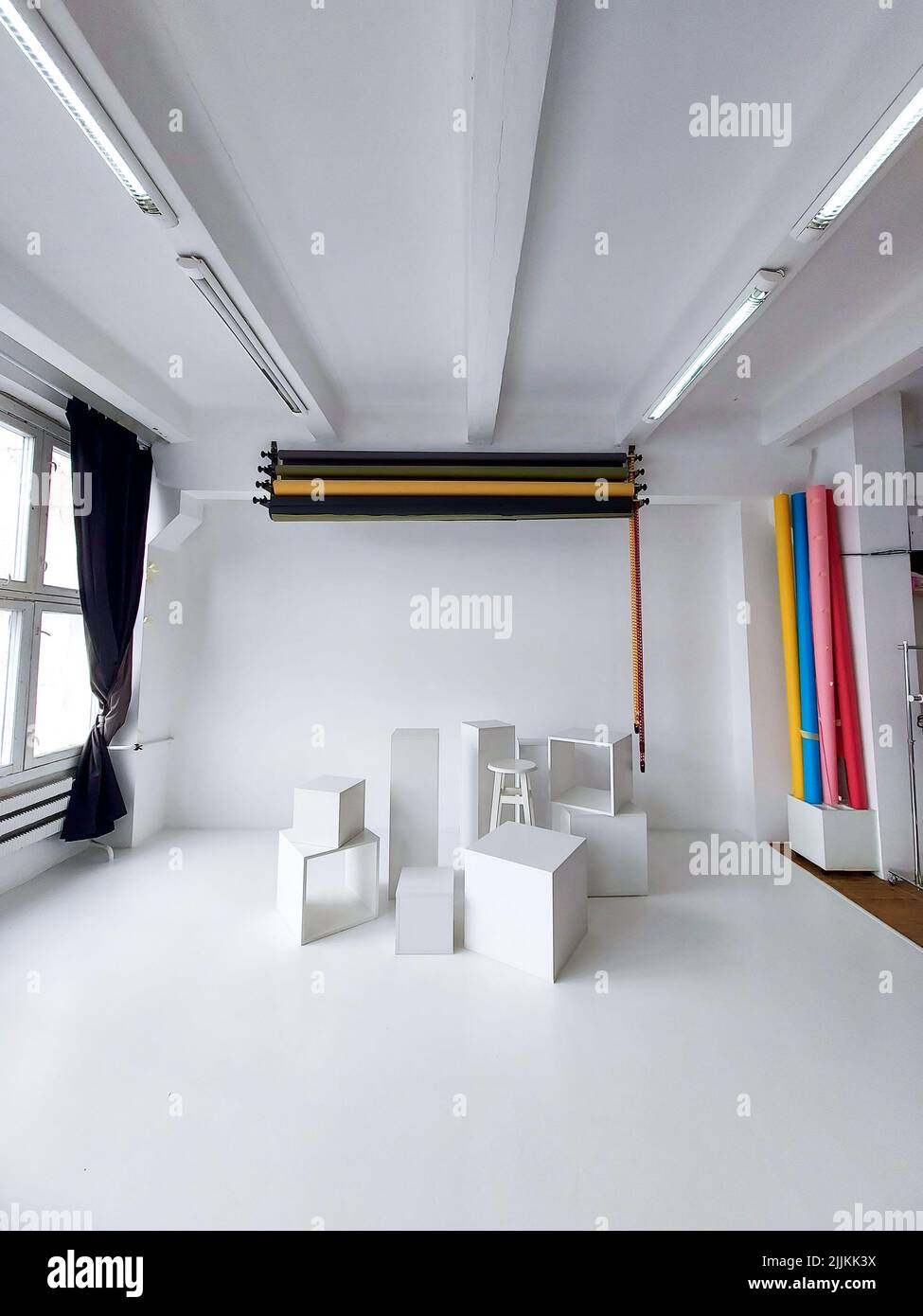 Intérieur de studio photo à la lumière du jour avec équipement professionnel sous forme de rouleaux d'arrière-plan de couleur et de cubes blancs sur un sol blanc. Banque D'Images