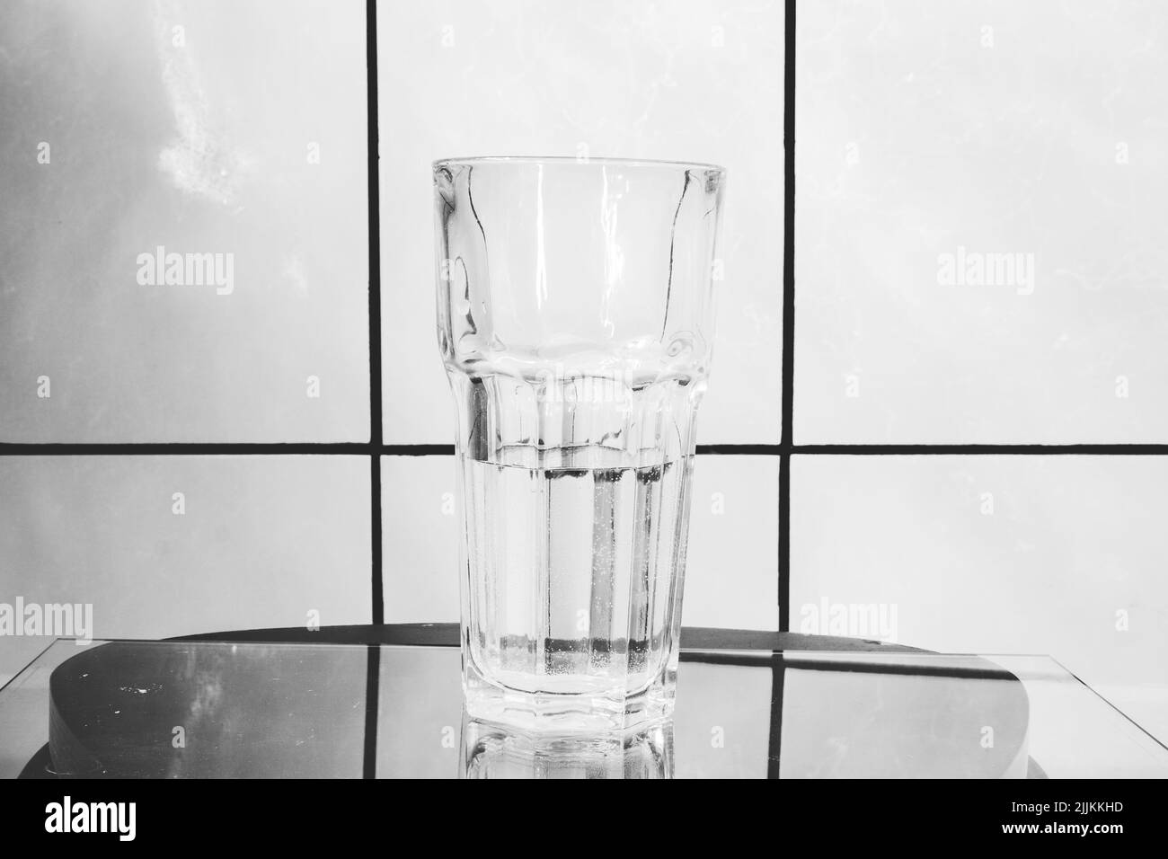 Verre de cristal pour les cocktails avec de l'eau sur la surface de verre. En arrière-plan carreaux blancs avec des joints noirs. Banque D'Images