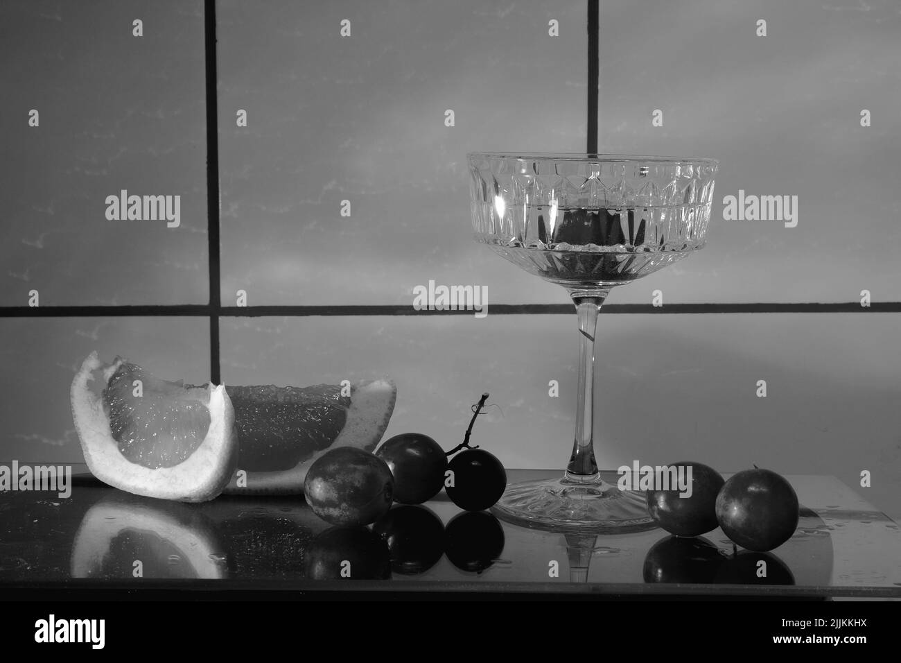 Verre en cristal pour des cocktails sur une surface en verre. Fruits - raisins, pamplemousse à côté du verre. Arrière-plan abstrait. Banque D'Images