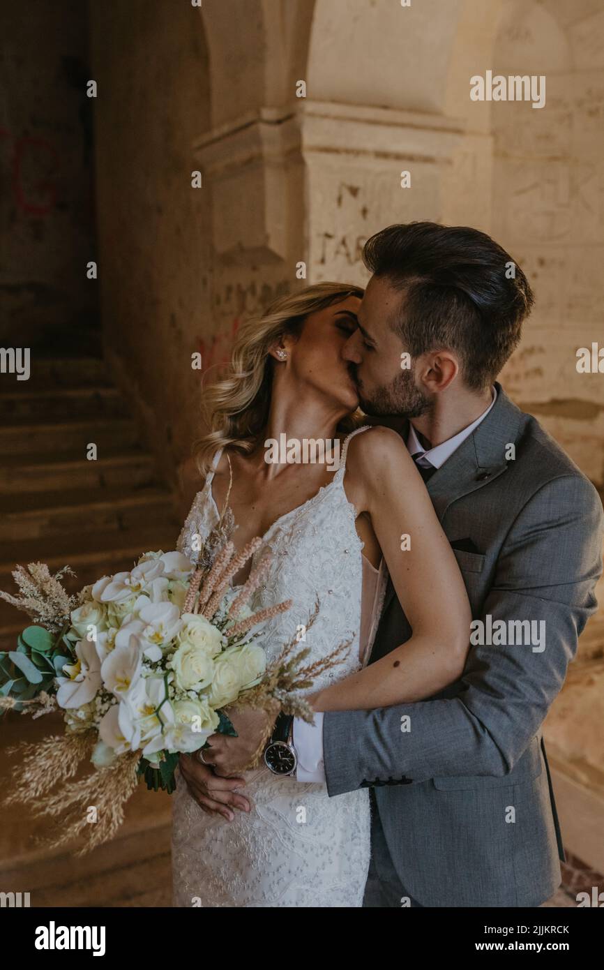 Une verticale d'un couple caucasien et moyen-oriental embrassant, tenant un bouquet sur leur mariage Banque D'Images