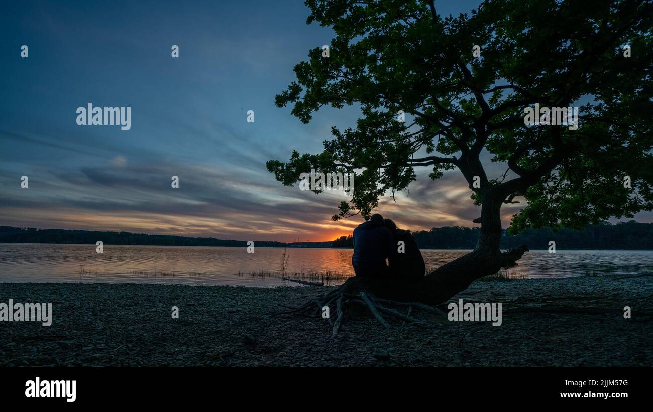 Un couple assis sur la plage appréciant la belle vue du coucher du soleil Banque D'Images