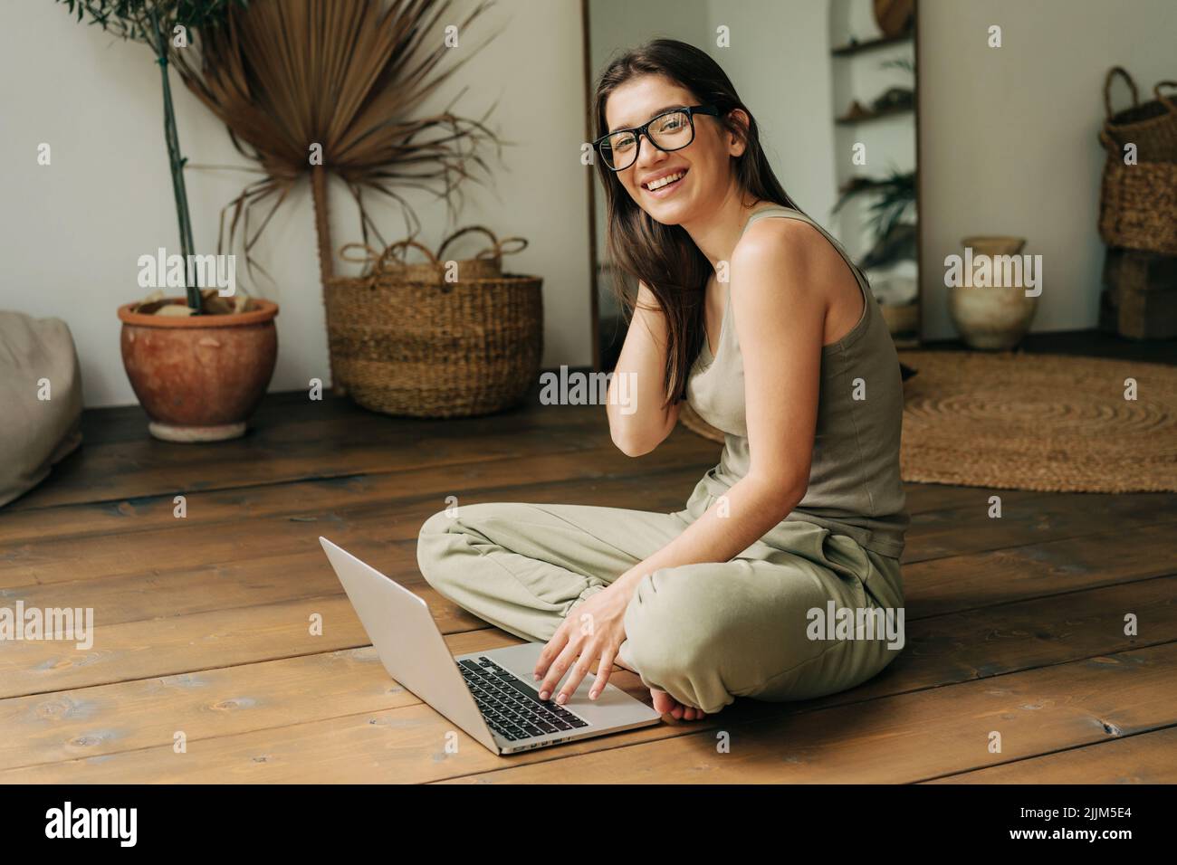 Jeune fille de brunette ethnique assise sur le sol travaillant sur un ordinateur portable. Banque D'Images