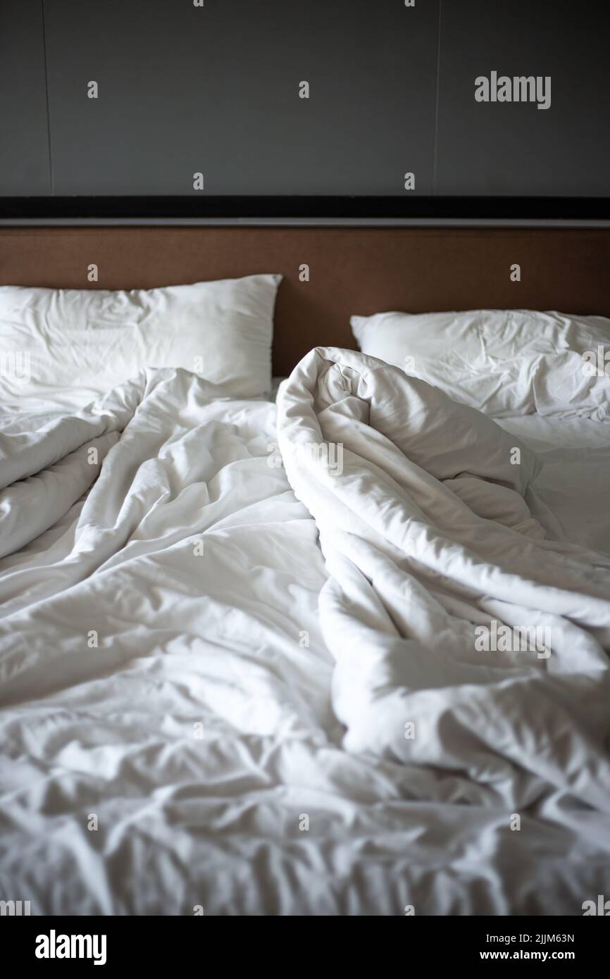 Vider un lit blanc froissé avec une couverture et des oreillers dans une pièce sombre le matin. Concept de vie familiale. Banque D'Images