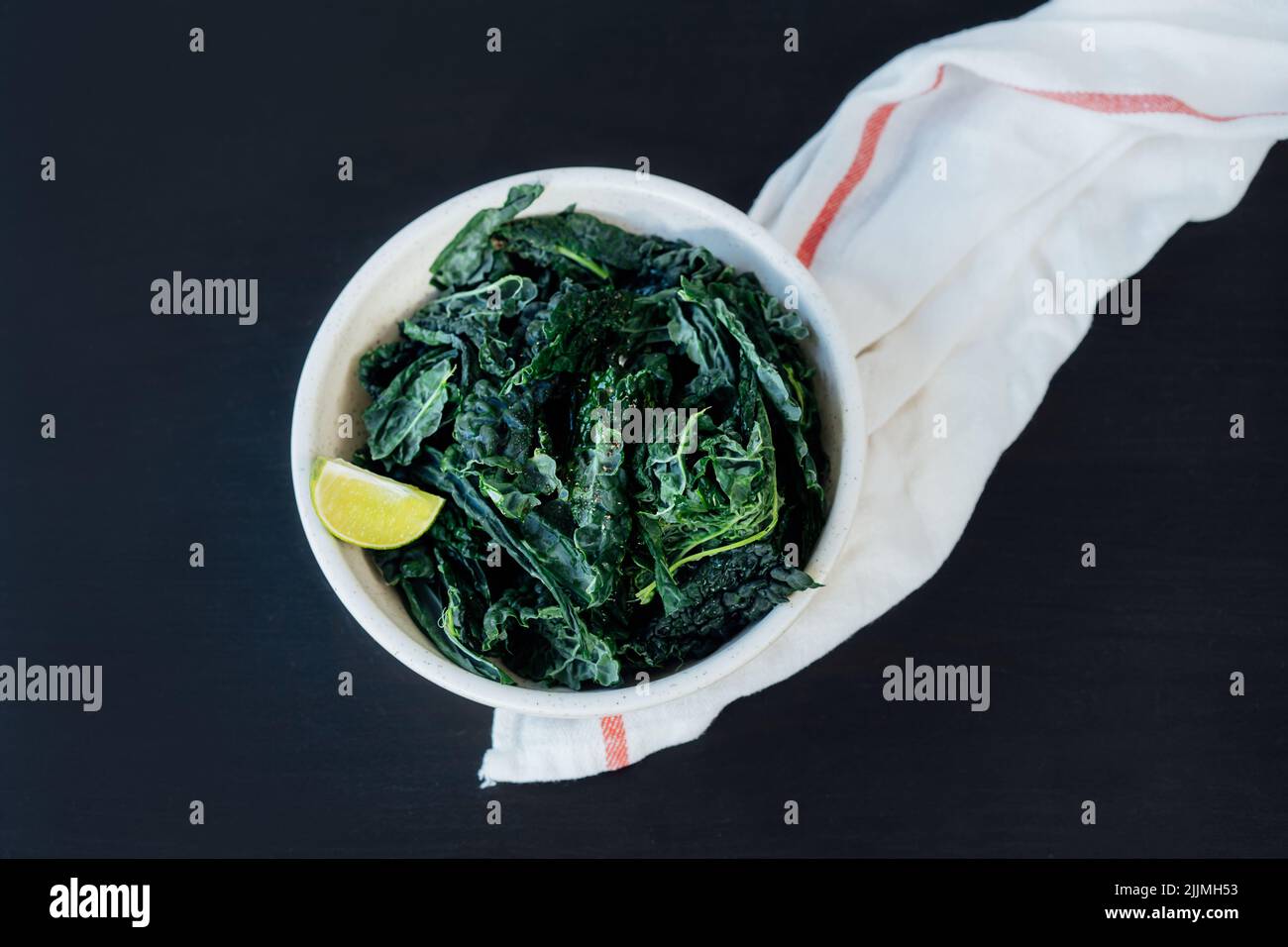 Vue de dessus des feuilles de kale vert poêlées dans l'assiette avec des assaisonnements et de l'huile d'olive sur la table de cuisine. Ingrédients pour des chips de chou frisé ou une salade saine m Banque D'Images Vue de dessus des feuilles de kale vert poêlées dans l'assiette avec des assaisonnements et de l'huile d'olive sur la table de cuisine. Ingrédients pour des chips de chou frisé ou une salade saine m Banque D'Images
