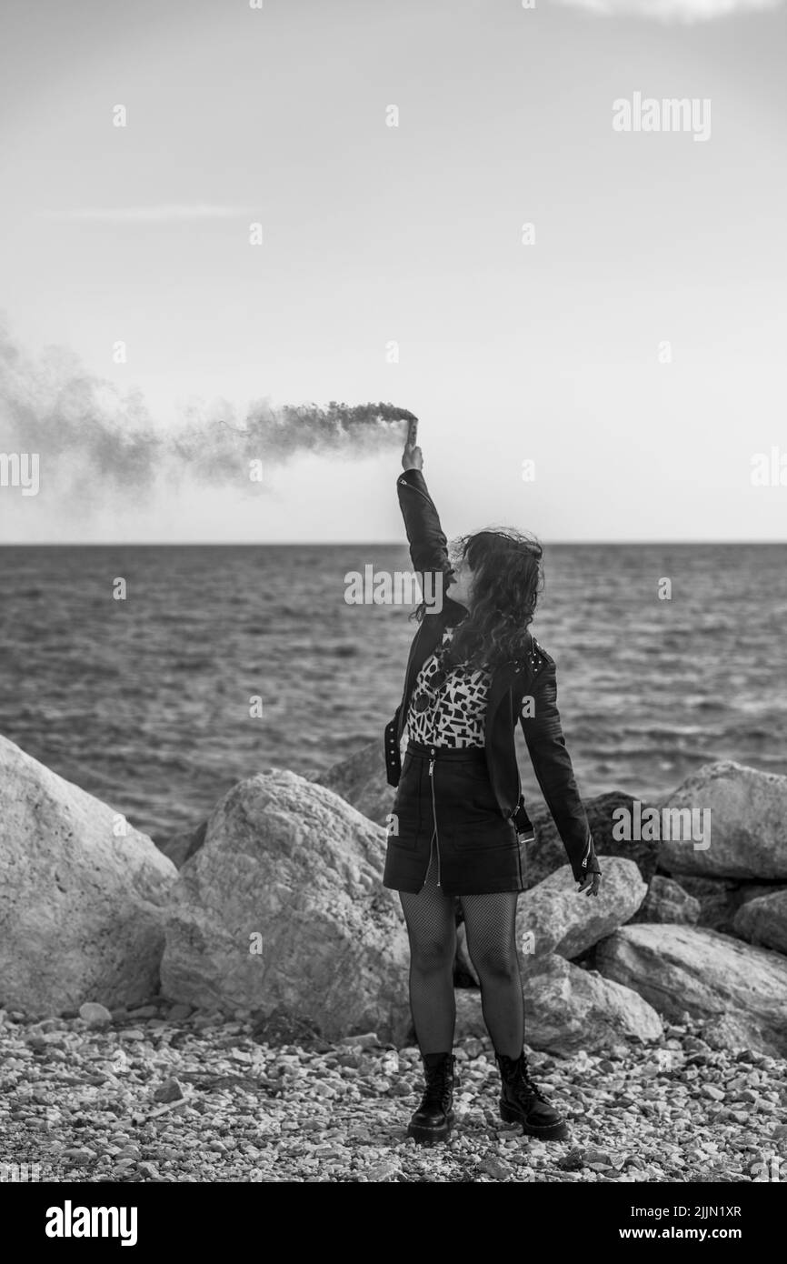 Une belle photo en niveaux de gris d'une fille caucasienne jouant avec de la fumée colorée dehors avec des rochers Banque D'Images