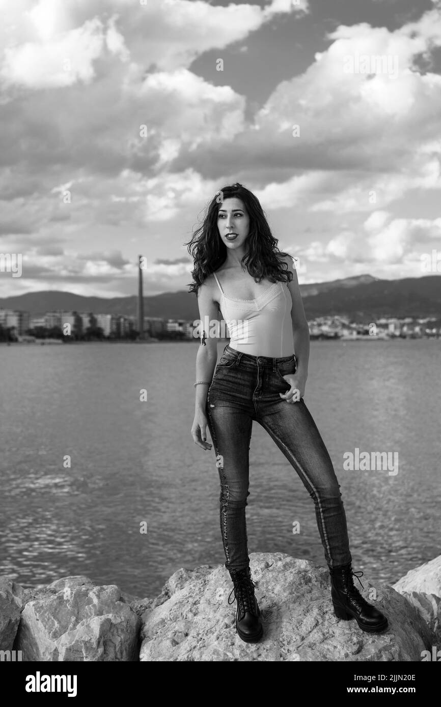 Photo verticale en niveaux de gris d'une femme caucasienne debout sur un rocher en arrière-plan d'un lac. Banque D'Images