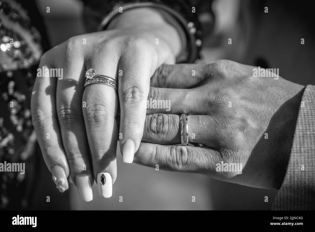 Un gros plan en niveaux de gris des mains de la jeune mariée et du marié avec les anneaux. Banque D'Images