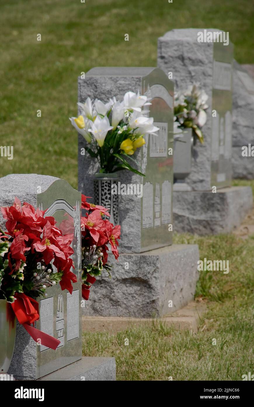 La photo latérale de pierres à tête avec des fleurs dans un cimetière. Banque D'Images