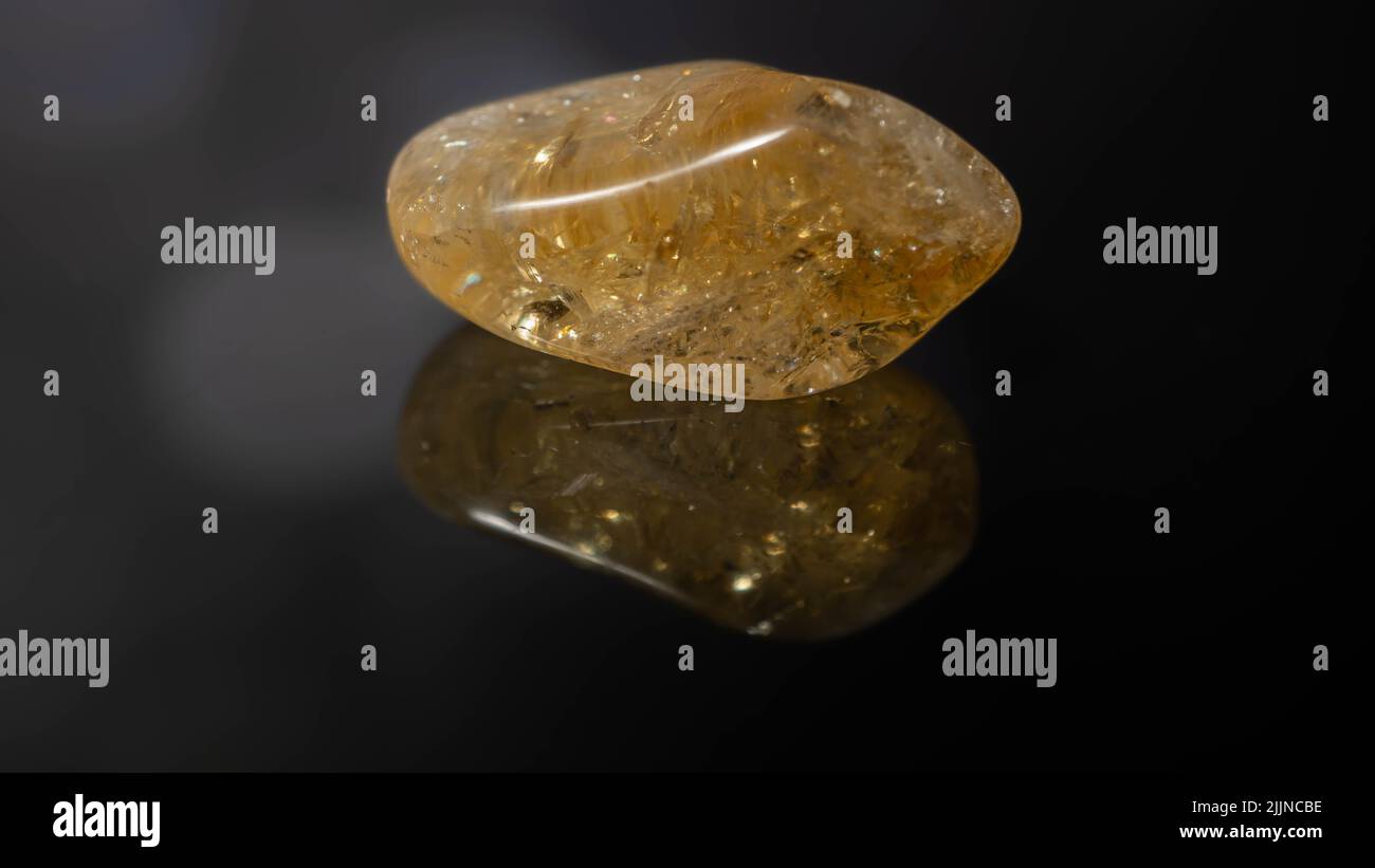Un gros plan d'une pierre précieuse naturelle - galet de pierre précieuse minérale citrine sur une surface réfléchissante Banque D'Images