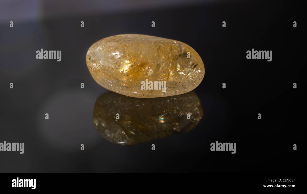 Un gros plan d'une pierre précieuse naturelle - galet de pierre précieuse minérale citrine sur une surface réfléchissante Banque D'Images