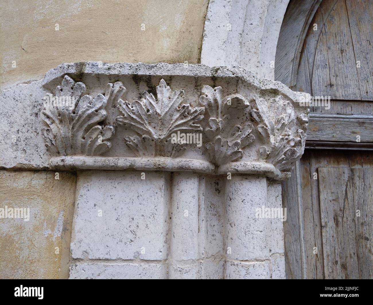 Un gros plan d'une sculpture en pierre antique sur un vieux bâtiment blanc avec une porte en bois Banque D'Images