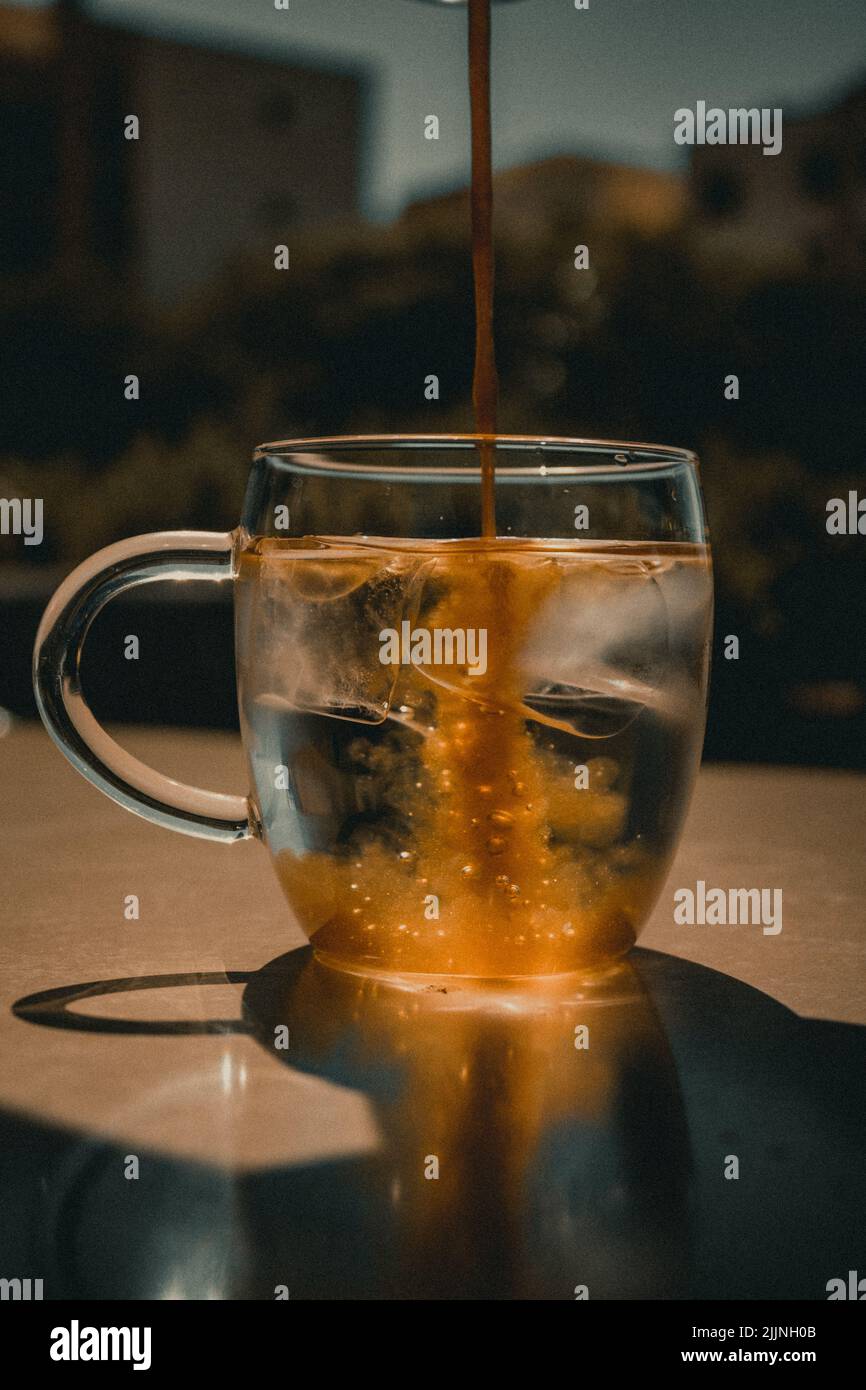 Une verticale de café versé dans la tasse en verre remplie de glaçons Banque D'Images