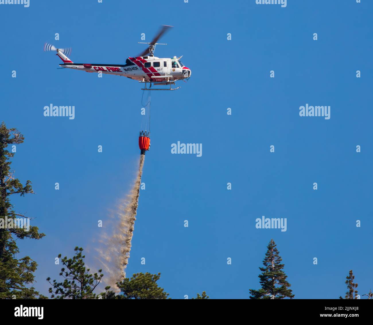 CALFIRE UH-1 hélicoptère larguer de l'eau sur un petit feu de forêt près de la ligne du comté de Plumas/Lassen, Californie, États-Unis... Banque D'Images