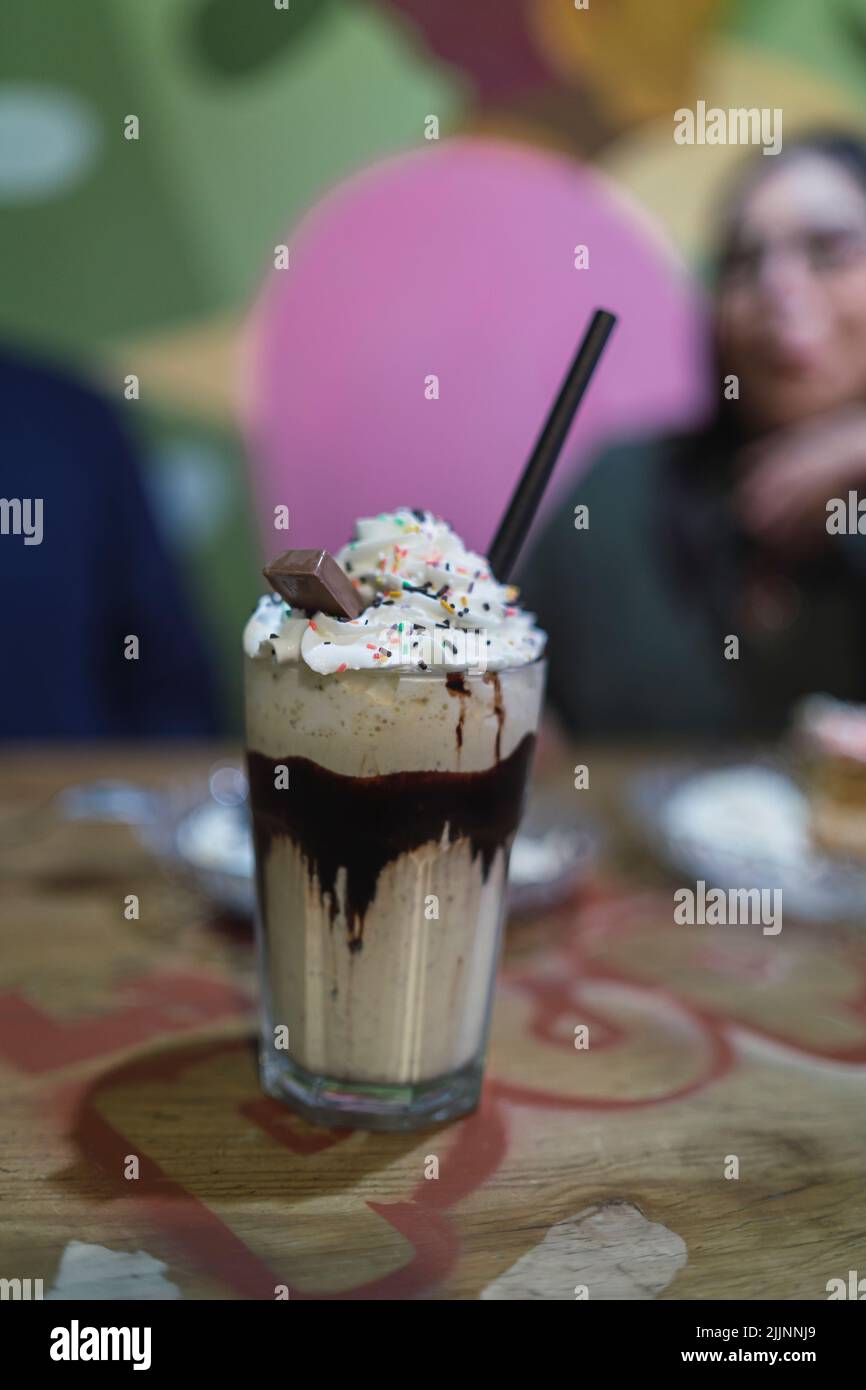 Un gros plan d'une tasse de milkshake avec une paille noire sur la table avec une fille souriante dans l'arrière-plan flou Banque D'Images