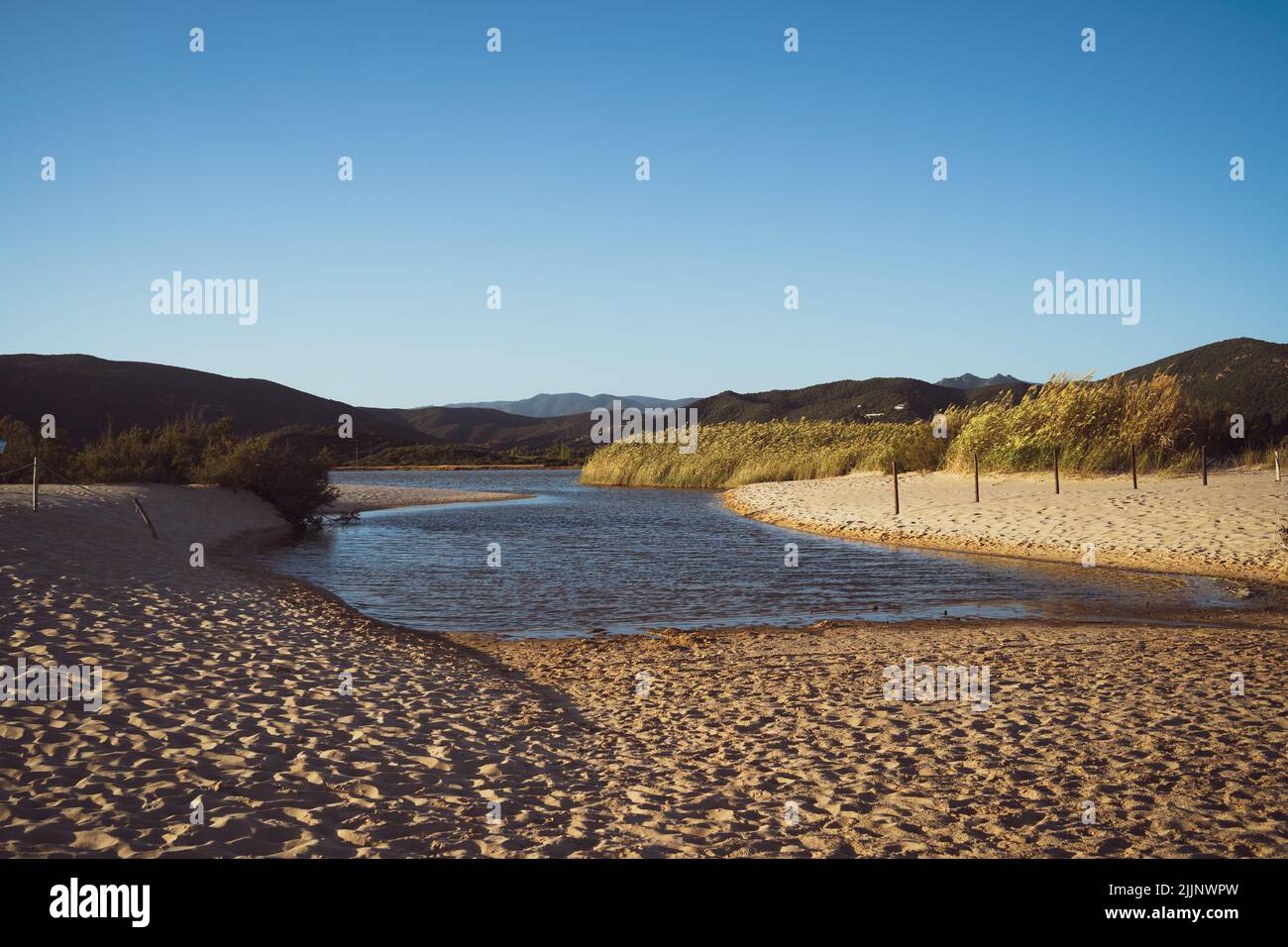 Une vue sur la plage de sable de Chia avec des empreintes de pieds dans le fond de collines verdoyantes Banque D'Images