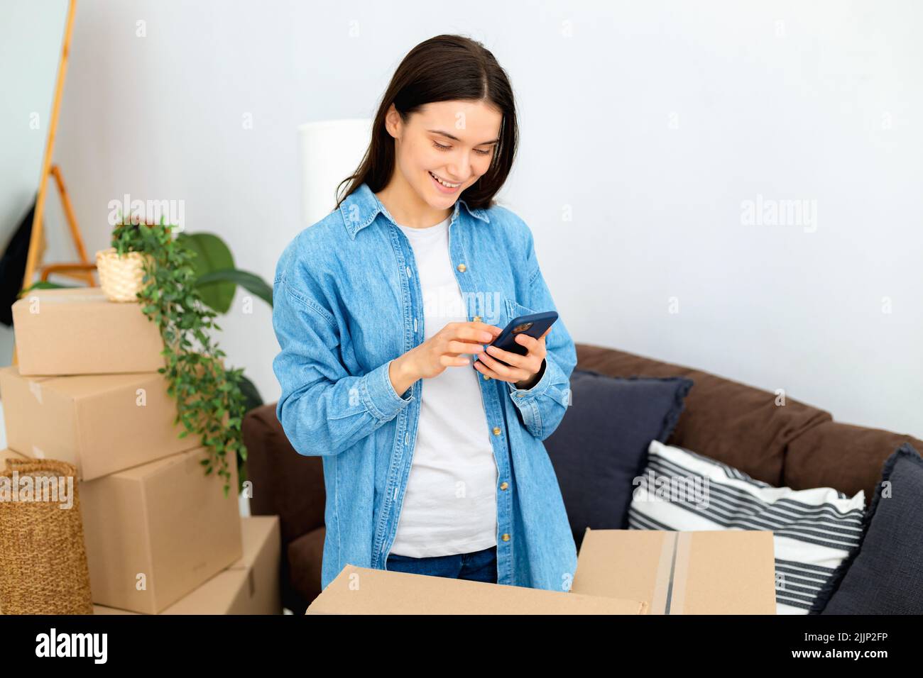 Une jeune femme heureuse utilisant le service de transport de commande de téléphone mobile et les déménageurs pour déménager à la maison nouvelle Banque D'Images