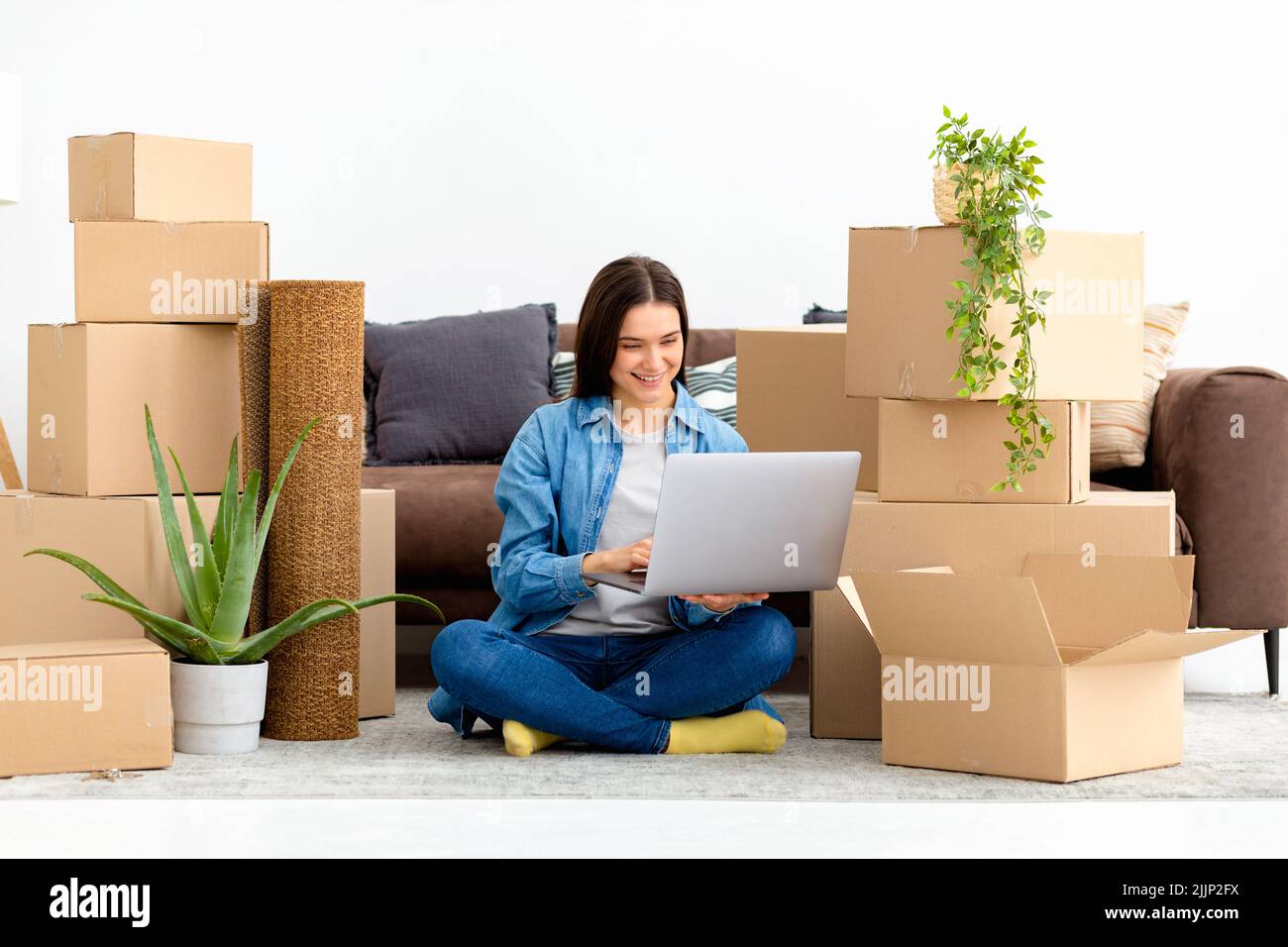 Déménagement dans une nouvelle maison, logement de location. Bonne femme utilisant un ordinateur portable pour rechercher et commander le service de transport Banque D'Images