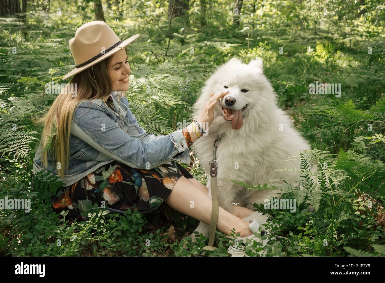 Jeune belle femme passant du temps avec son chien blanc moelleux samoyed dans la forêt Banque D'Images