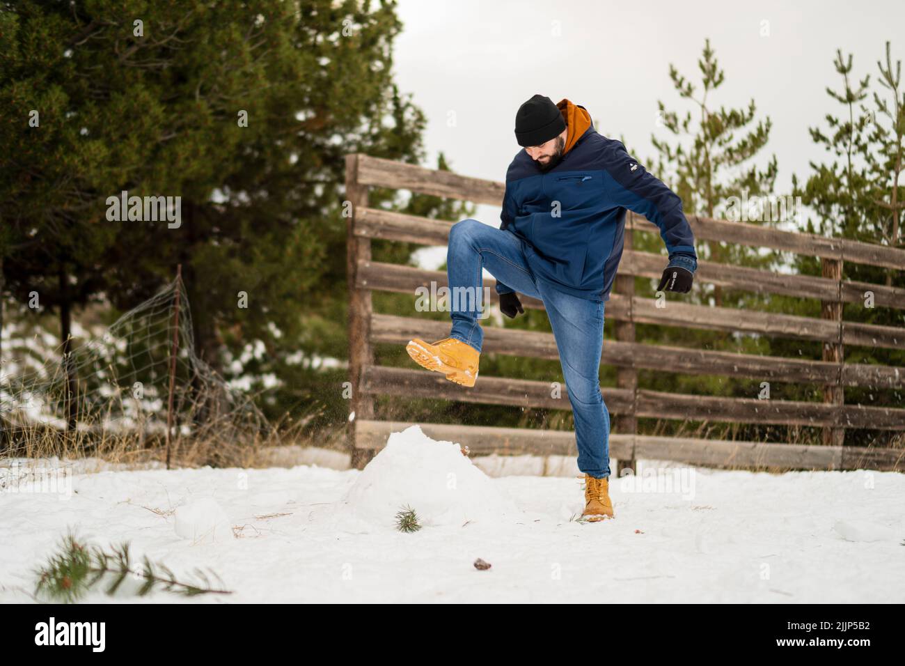 Un jeune caucasien écrasant la neige avec son pied dans le parc pendant l'hiver Banque D'Images