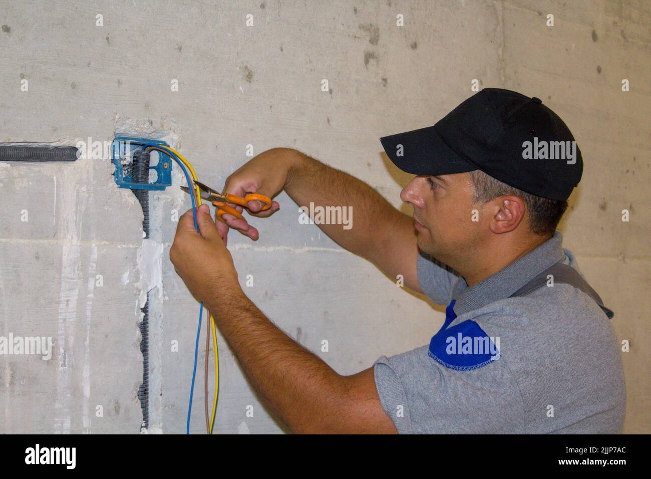 Image d'un électricien de main coupant des câbles d'alimentation avec une paire de ciseaux. Réalisation d'un système électrique d'une maison. Banque D'Images