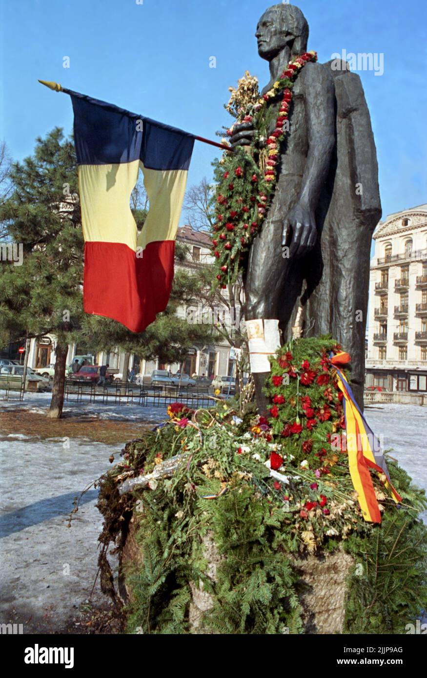 Bucarest, Roumanie, janvier 1990. Quelques semaines après la révolution roumaine de 1989, des fleurs sont placées autour de la statue du poète national Mihai Eminescu, devant l'Athenaeum. Le drapeau national avec l'emblème socialiste coupé est devenu un symbole pendant la révolution, représentant la fin de l'ère communiste. Banque D'Images