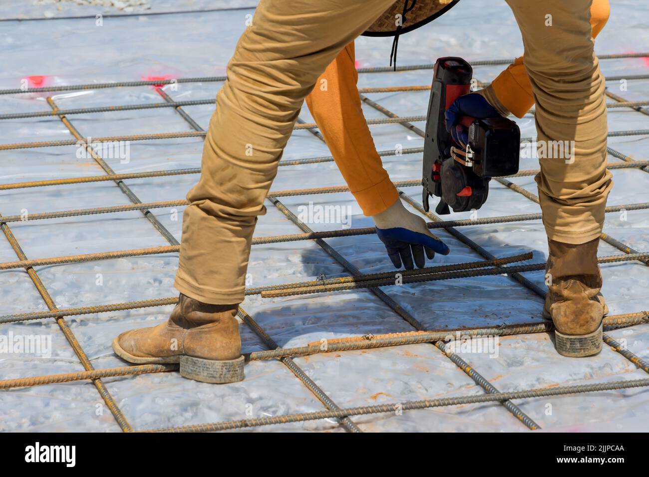 L'ouvrier de construction tord les barres d'acier avec le renforcement de la tige de fil pour la fondation d'un bâtiment de ciment en utilisant un outil appelé un rembaring Banque D'Images