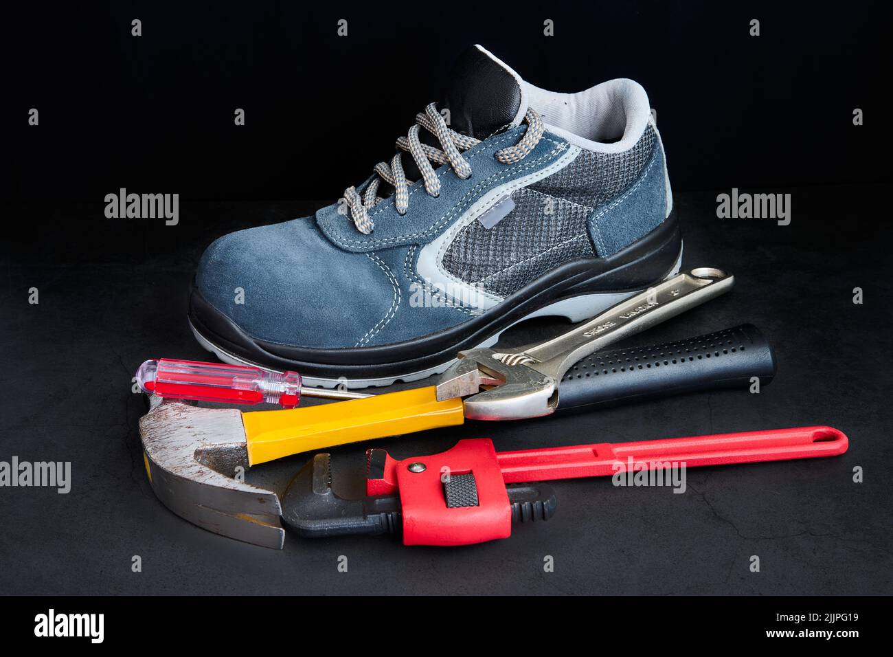 Un gros plan de la chaussure d'un homme avec des outils de construction colorés à côté sur un fond noir Banque D'Images